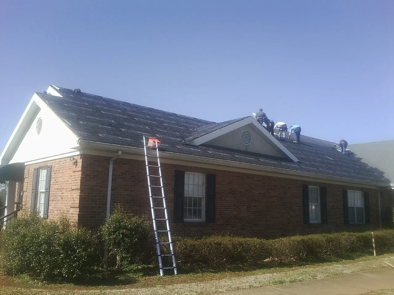 Crew tearing shingles off a brick ranch roof with a ladder set — Metal Roof Repair work by our crew in Cleaton