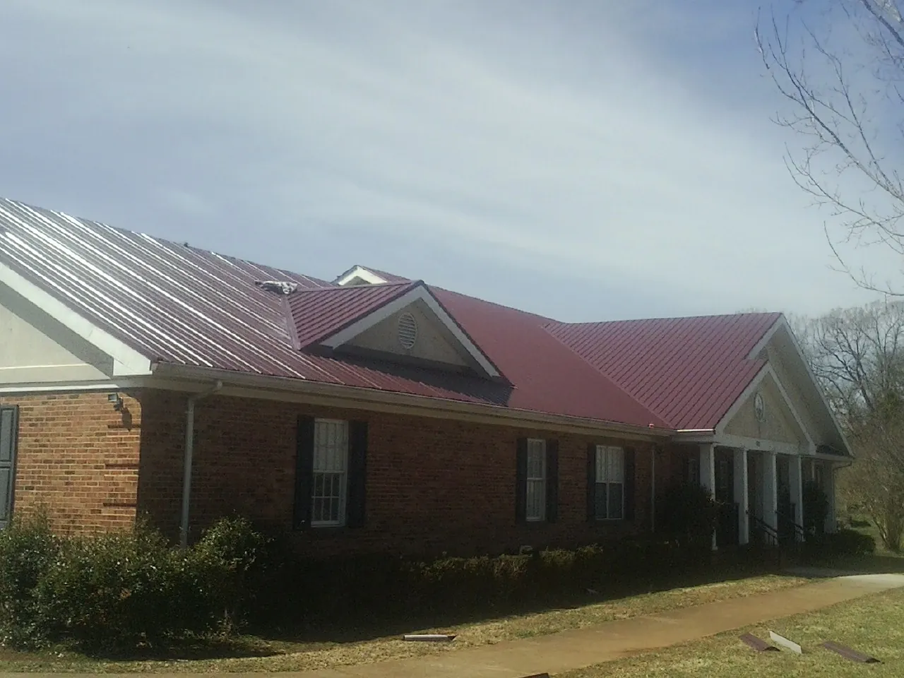 Red metal roof with gabled entries on a long brick building, from a Hail Damage Roof Repair job in Cleaton