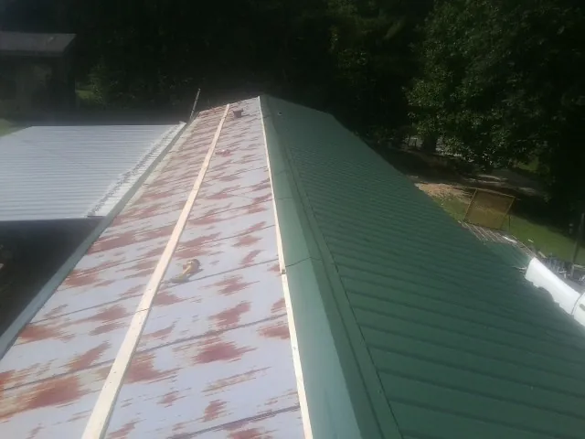 Old rusted panels beside newly installed green metal roofing — Wind Damage Roof Repair by Roofing Brothers in Cleaton