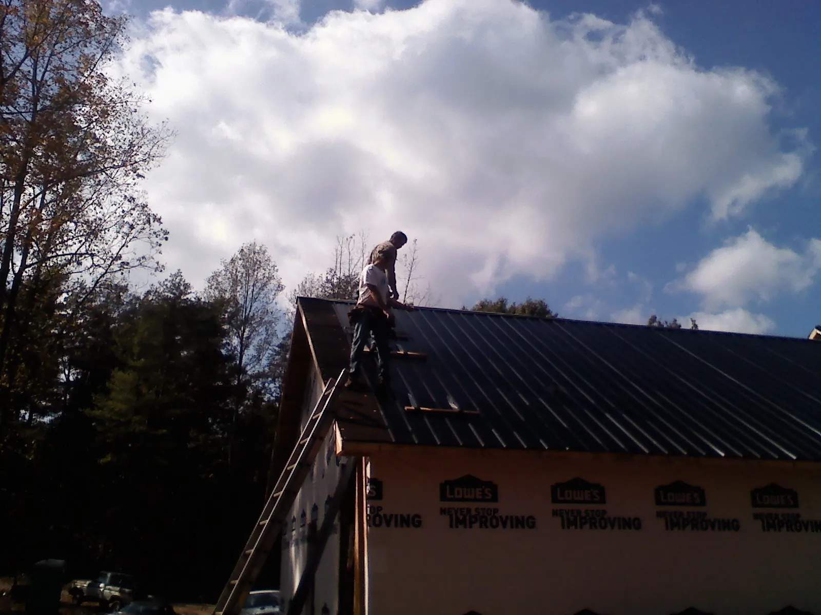 Roofer fastening dark metal panels high against a cloudy sky, from a Roof Inspection job in Cleaton